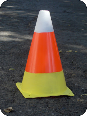 A traffic cone painted in yellow, orange, and white, resembling a candy corn.